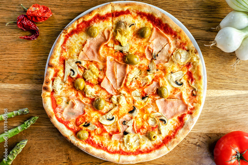 Quattro Staggioni pizza with olives, artichockes and ham served on a wooden table in trattoria italiana #397845968