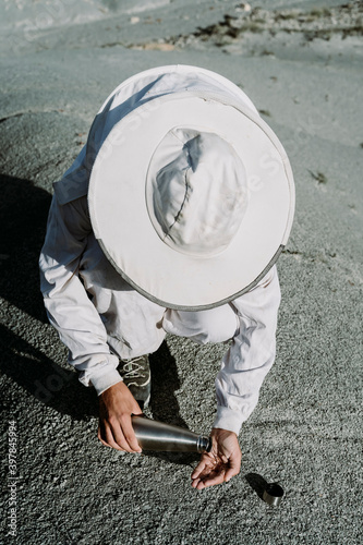 Man with thermos flask wearing a beekeeper dress in an arid landscape