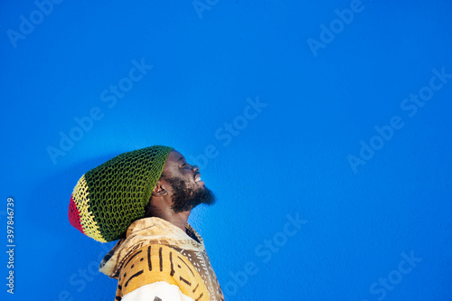 Portrait of Rastafai man with dreadlock cap against blue background