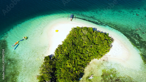 Small Island with beautiful beach, palm trees by turquoise water view from above. Britania Islands, Surigao del Sur, Philippines.