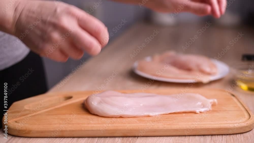 Female hands grease chicken breast with olive oil on a wooden cut board on the kitchen. Cooking chicken breast at home. Close up. Female hands grease chicken breast with olive oil on a wooden cut board on the kitchen. Cooking chicken breast at home. Close up.