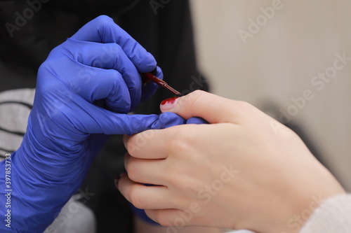 Master in protective gloves during a manicure at beauty salon. Master manicurist varnishes the marsala gel on the nails of a female client. The concept of beauty and health.