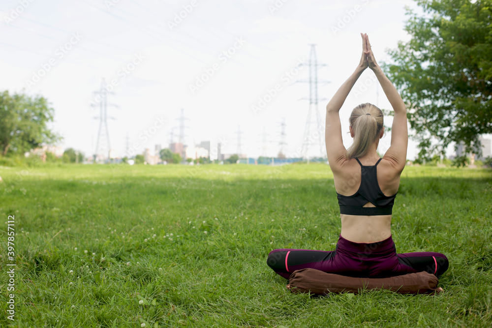 Fototapeta premium Woman doing yoga exercises outdoors. A beautiful sports girl is engaged in yoga on the background of beautiful nature.