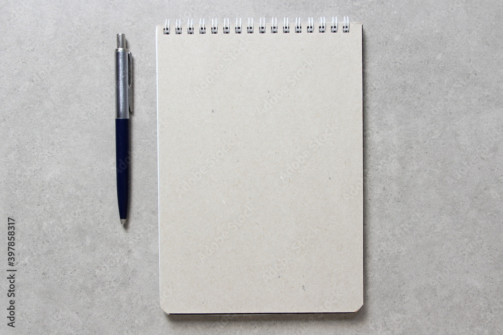 A spring notebook with a sheet of craft paper A5 with a ballpoint pen on light grey concrete background. Concept of new idea, business plan and strategy. Empty space for text A spring notebook with a sheet of craft paper A5 with a ballpoint pen on light grey concrete background. Concept of new idea, business plan and strategy. Empty space for text