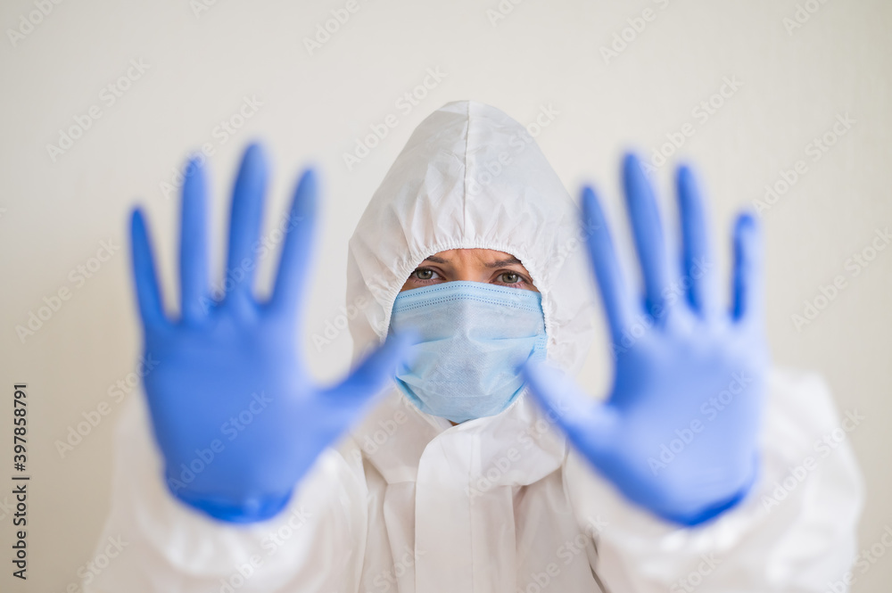 Woman in protective suit, medical mask and latex gloves, shows stop gesture. Tired doctor in the coronavirus epidemic Woman in protective suit, medical mask and latex gloves, shows stop gesture. Tired doctor in the coronavirus epidemic