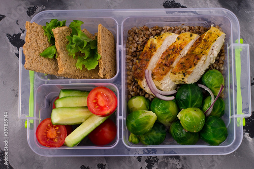 Healthy, diet food in boxes. Chicken fillet, buckwheat porridge, Brussels sprouts, tomatoes, cucumbers, bread. On a gray background. Top view