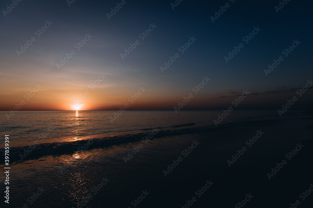 Breathtaking summer sunset view on the beach. Wonderful sunset landscape at the deep dark sea and orange sky above it and calm waves are flowing on it.