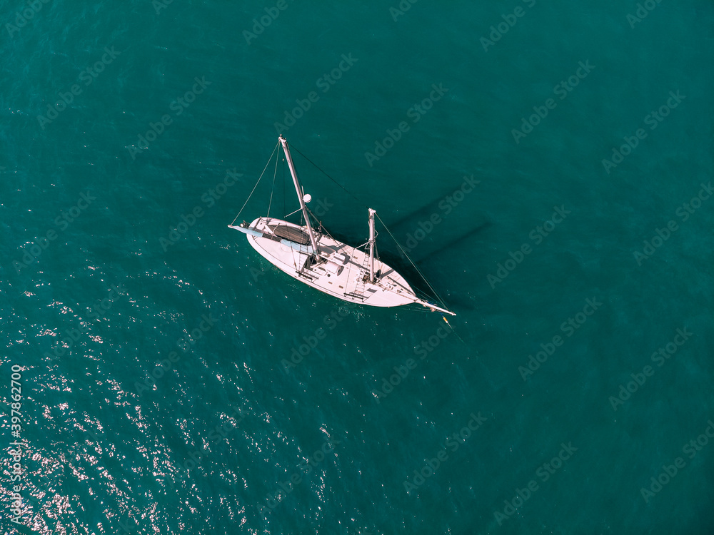 Small sail boat is sailing across the deep emerald sea. Aerial view.