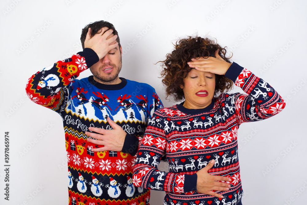 Young couple wearing Christmas sweater standing against white wall Touching forehead for illness and fever, flu and cold, virus sick.