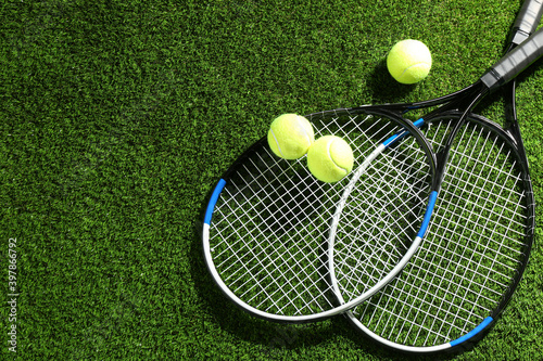 Tennis rackets and balls on green grass, flat lay. Space for text