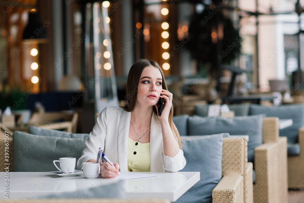 Young woman in white jacket working in cafe with papers, drinking coffee Young woman in white jacket working in cafe with papers, drinking coffee