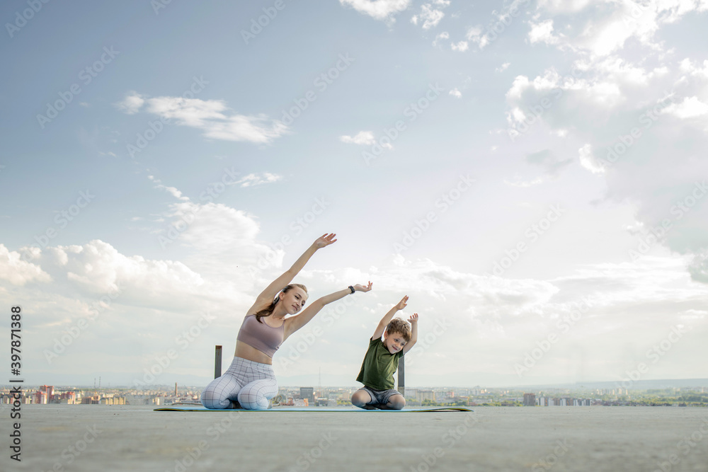 Mother and son doing exercise on the balcony in the background of a city during sunrise or sunset, concept of a healthy lifestyle Mother and son doing exercise on the balcony in the background of a city during sunrise or sunset, concept of a healthy lifestyle