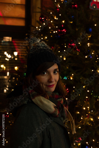 Portrait of an attractive young female posing next to a Christmas tree decorated with lights and figures