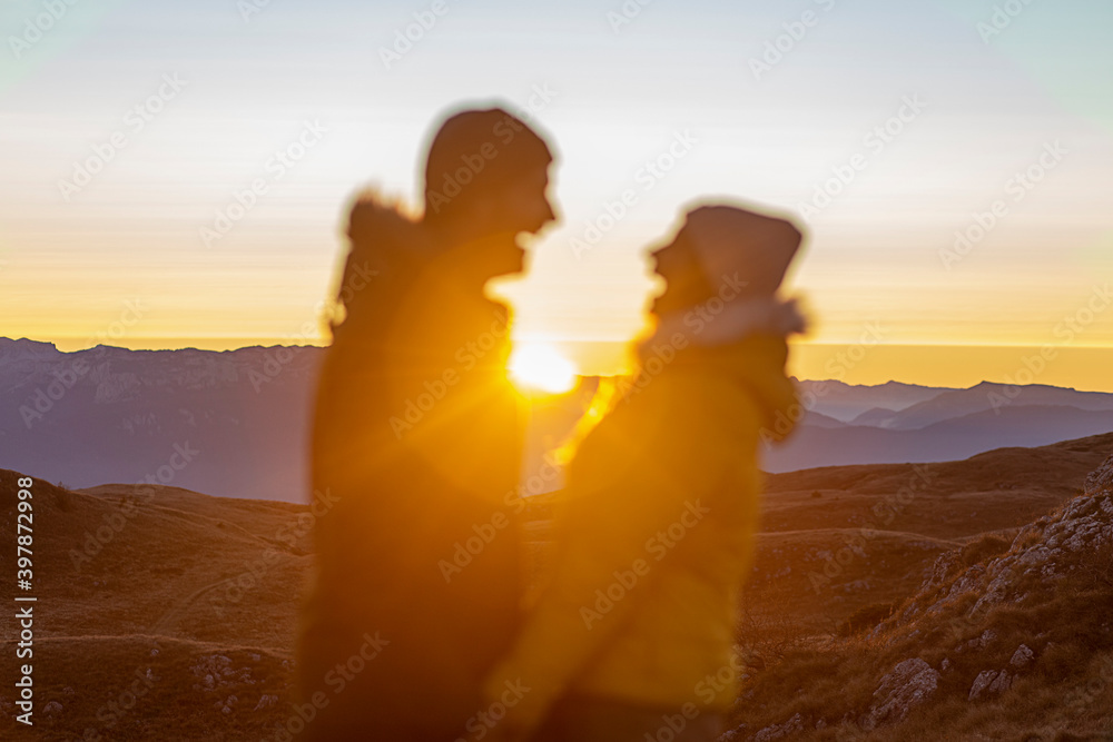 A young funny couple is enjoying the sunset at the top of the mountain. 