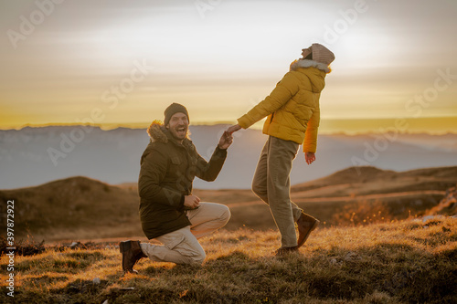Young man making a marriage proposal to his girlfriend on the mountain peak at sunset. 