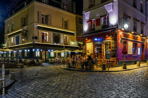 Fototapeta Naklejka Na Ścianę i Meble -  Typical night view of cozy street with tables of cafe and easels of street painters in quarter Montmartre in Paris, France