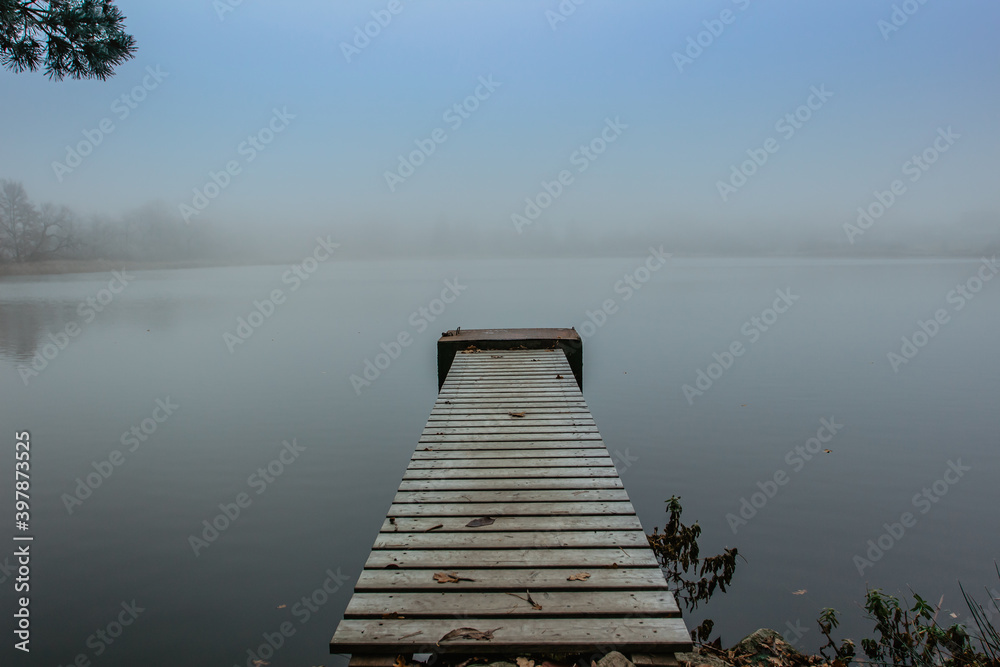 Mysterious morning by lake. Foggy autumn mystery atmosphere. Wooden pier on the pond.Magic mood. Misty fall day. Speechless place. Relaxing meditation without people.Silence scene.Serenity background.