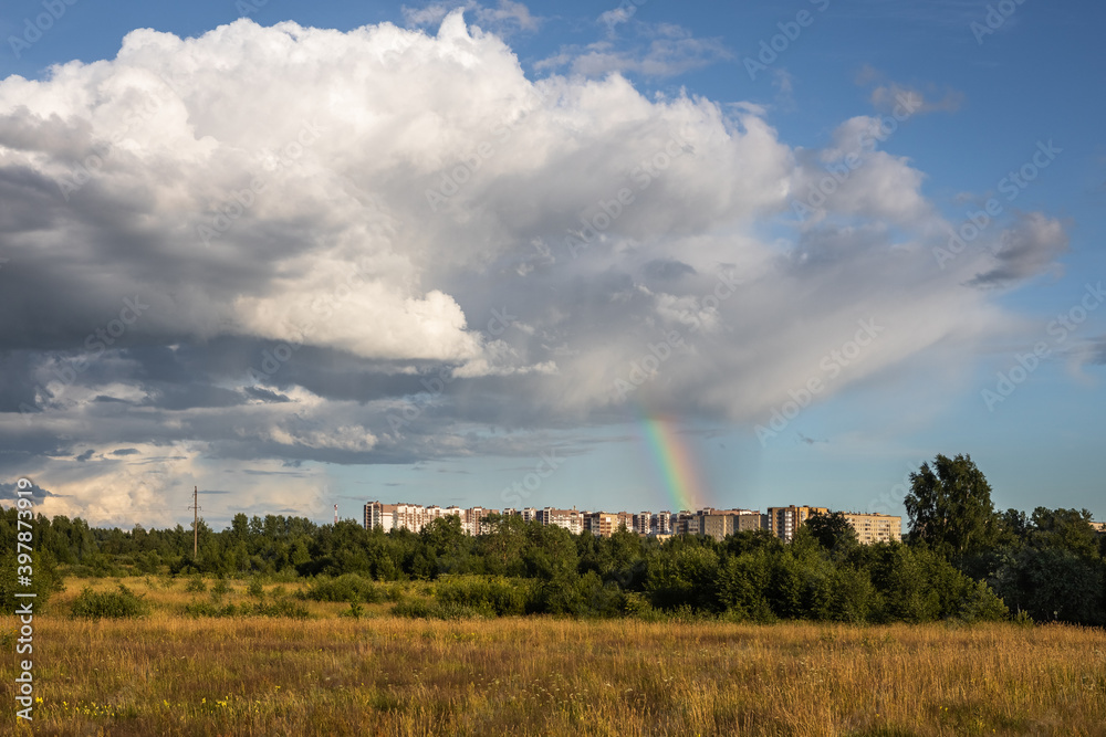 View of the city blocks from the side of the field. There is a big cloud and a rainbow in the sky.