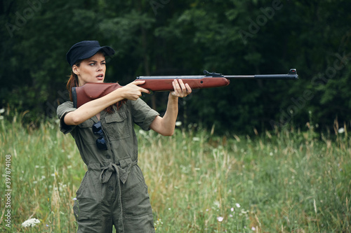 Woman soldier with a gun in hand takes aim green overalls green trees 