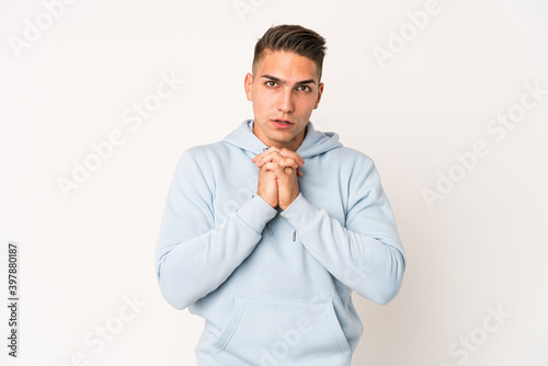 Young caucasian handsome man isolated praying for luck, amazed and opening mouth looking to front.