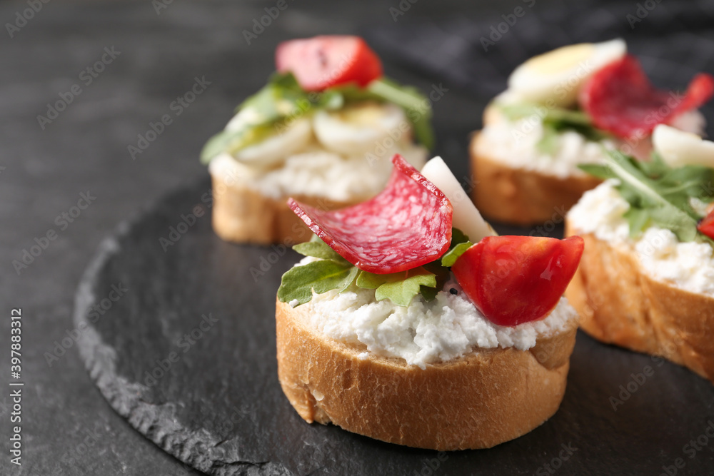 Delicious bruschettas with sausage and cheese on black table, closeup