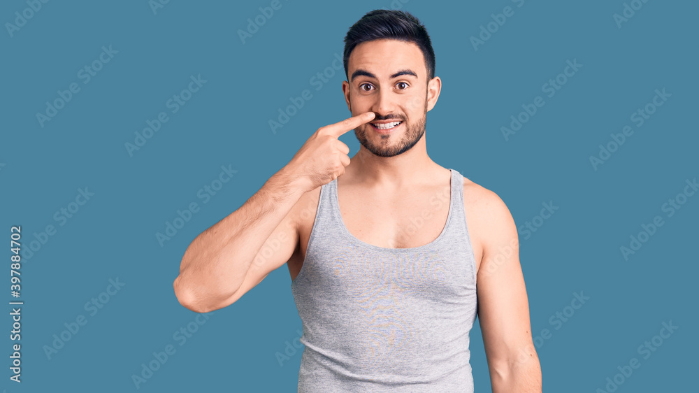 Young handsome man wearing swimwear and sleeveless t-shirt pointing with hand finger to face and nose, smiling cheerful. beauty concept Young handsome man wearing swimwear and sleeveless t-shirt pointing with hand finger to face and nose, smiling cheerful. beauty concept