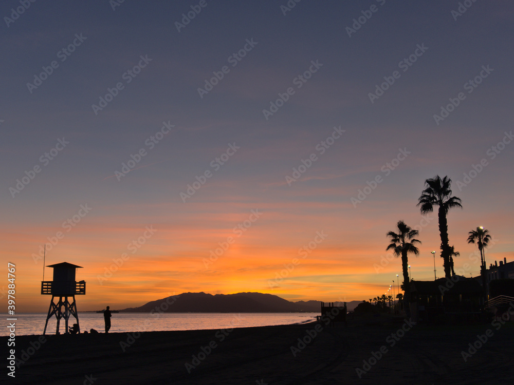 Silhouettes at sunset of a guard post and palms on the beach