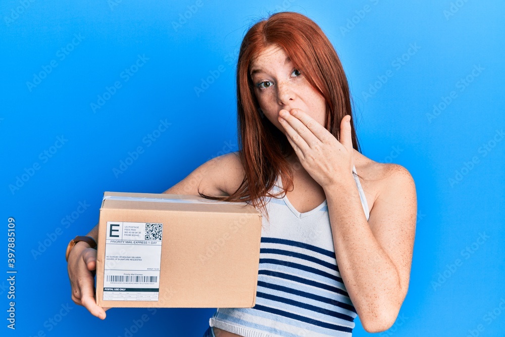 Young red head girl holding delivery package covering mouth with hand, shocked and afraid for mistake. surprised expression Young red head girl holding delivery package covering mouth with hand, shocked and afraid for mistake. surprised expression