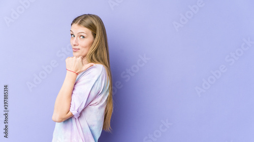 Young blonde woman isolated on purple background points with thumb finger away, laughing and carefree.