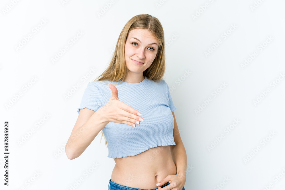 Young blonde woman isolated on white background stretching hand at camera in greeting gesture.