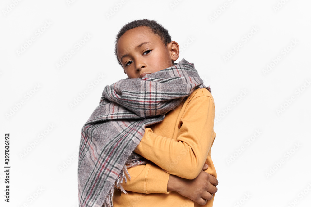 Children fashion, style, clothing and season concept. Isolated image of confident stylish dark skinned little boy wearing warm woolen scarf around his neck and yellow sweatshirt, having serious look Children fashion, style, clothing and season concept. Isolated image of confident stylish dark skinned little boy wearing warm woolen scarf around his neck and yellow sweatshirt, having serious look