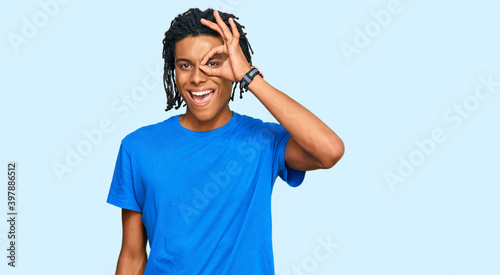 Fotografie Young african american man wearing casual clothes doing ok gesture with hand smiling, eye looking through fingers with happy face