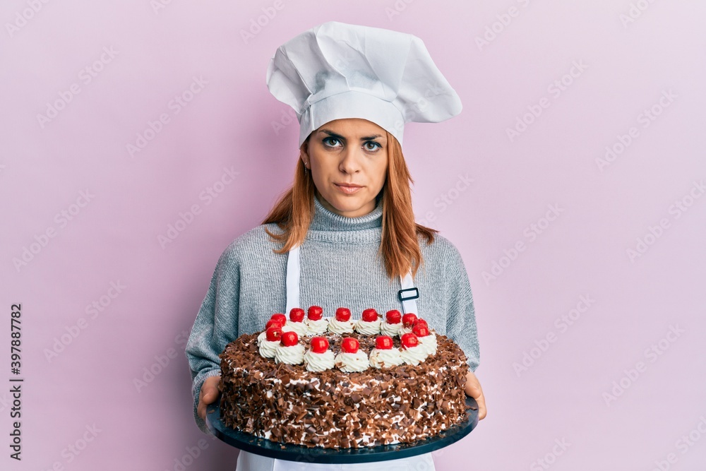 Hispanic young chef woman holding chocolate cake relaxed with serious expression on face. simple and natural looking at the camera. Hispanic young chef woman holding chocolate cake relaxed with serious expression on face. simple and natural looking at the camera.