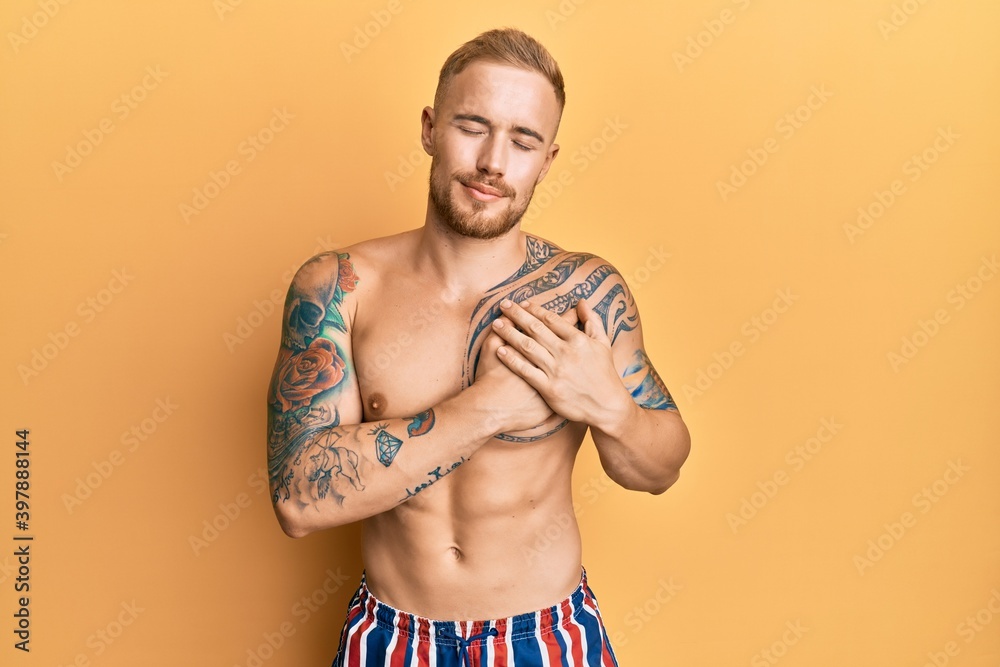 Fototapeta premium Young caucasian man wearing swimwear shirtless smiling with hands on chest with closed eyes and grateful gesture on face. health concept.