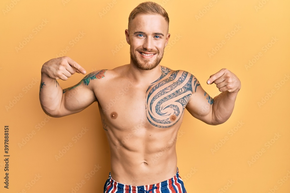 Young caucasian man wearing swimwear shirtless looking confident with smile on face, pointing oneself with fingers proud and happy.