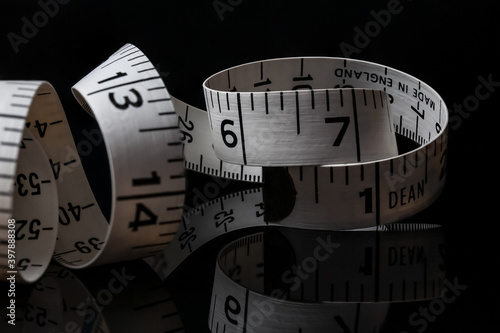 Dean measurement tape measure for tailor or seamstress coiled up on a reflective back surface in dramatic lighting. textiles industry clothing size