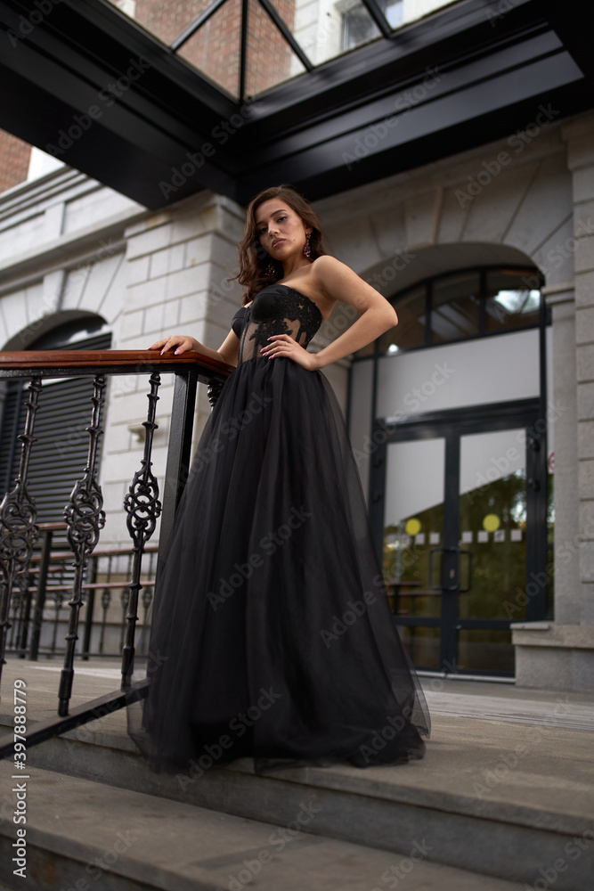 Full-length portrait of an elegant brunette woman with long hair in a black long evening dress.