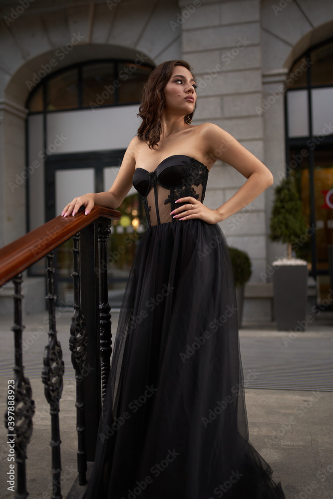 Full-length portrait of an elegant brunette woman with long hair in a black long evening dress.