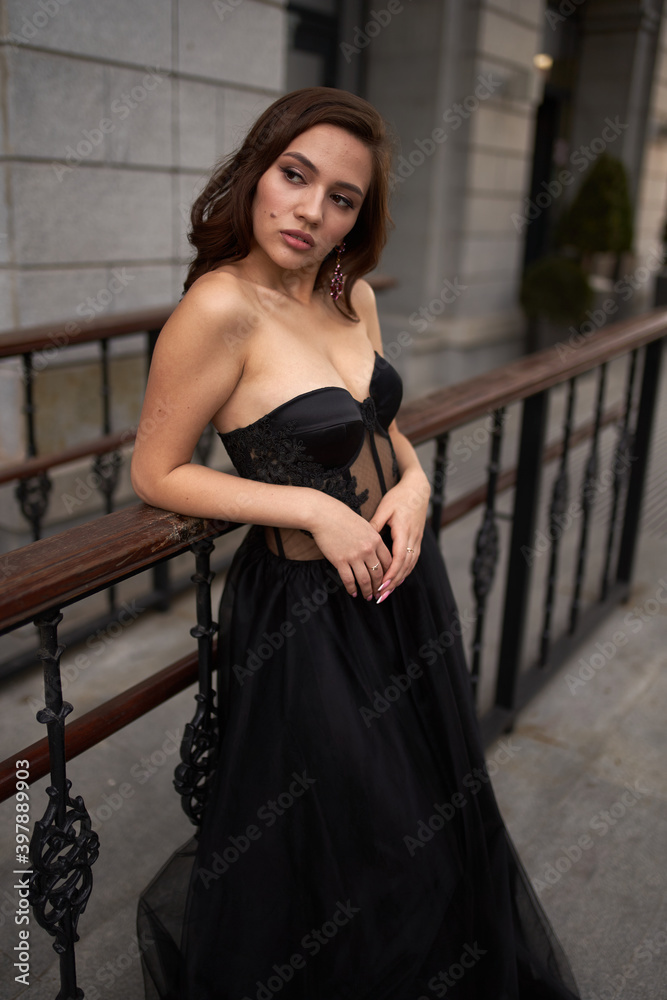 Fototapeta premium Full-length portrait of an elegant brunette woman with long hair in a black long evening dress.