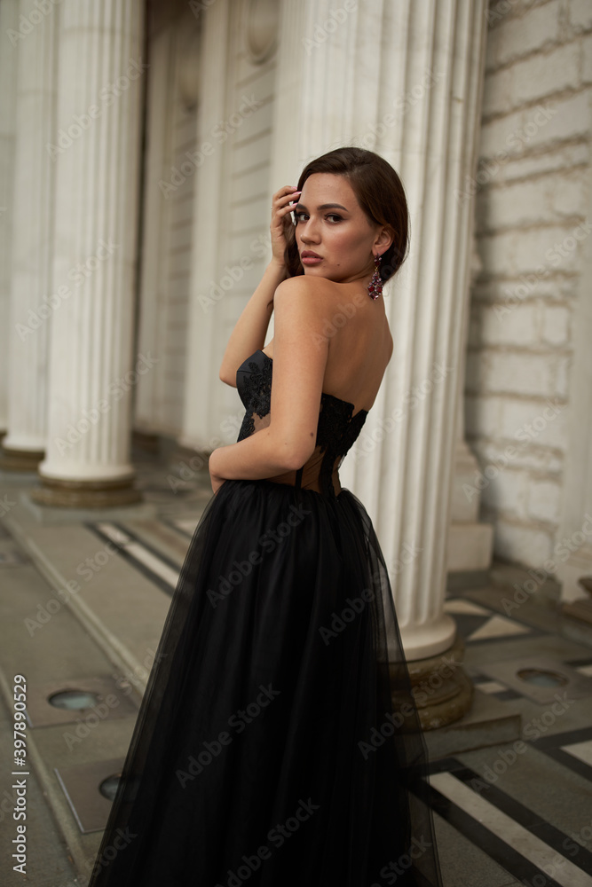 Full-length portrait of an elegant brunette woman with long hair in a black long evening dress.