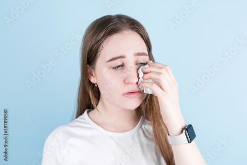 Portrait of displeased upset female crying over blue background.