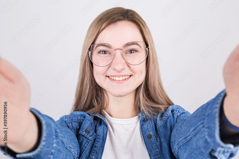 Pretty young girl with big smile having fun taking light cheerful selfie on gray background