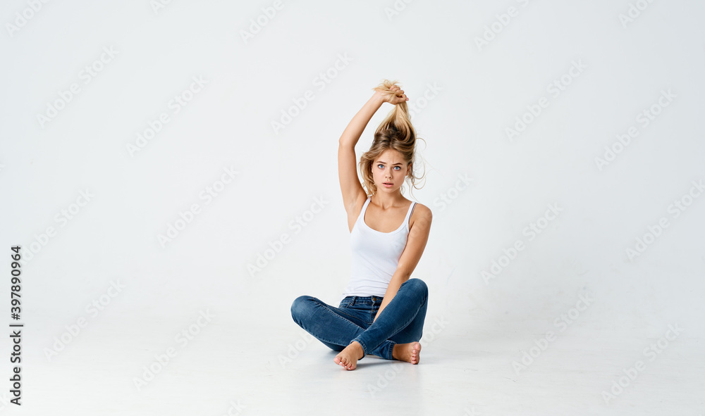 woman in jeans and white t-shirt touches hair on her head and sits on the floor indoors 