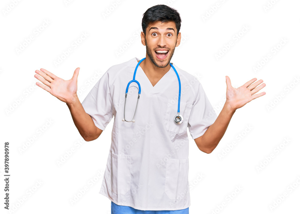 Young handsome man wearing doctor uniform and stethoscope celebrating victory with happy smile and winner expression with raised hands Young handsome man wearing doctor uniform and stethoscope celebrating victory with happy smile and winner expression with raised hands