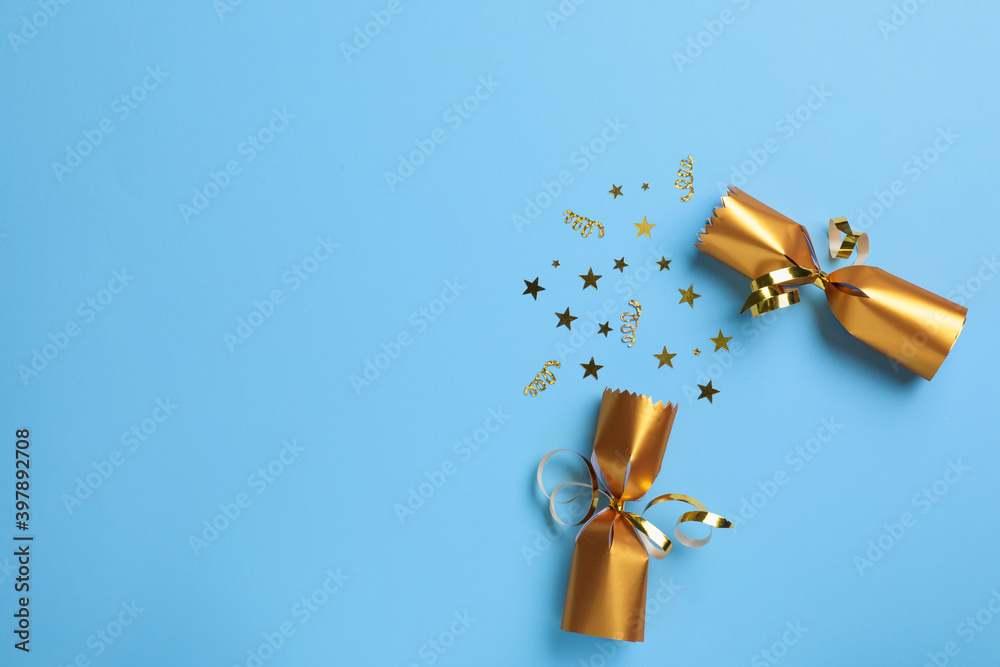 Open golden Christmas cracker with shiny confetti on light blue background, top view. Space for text