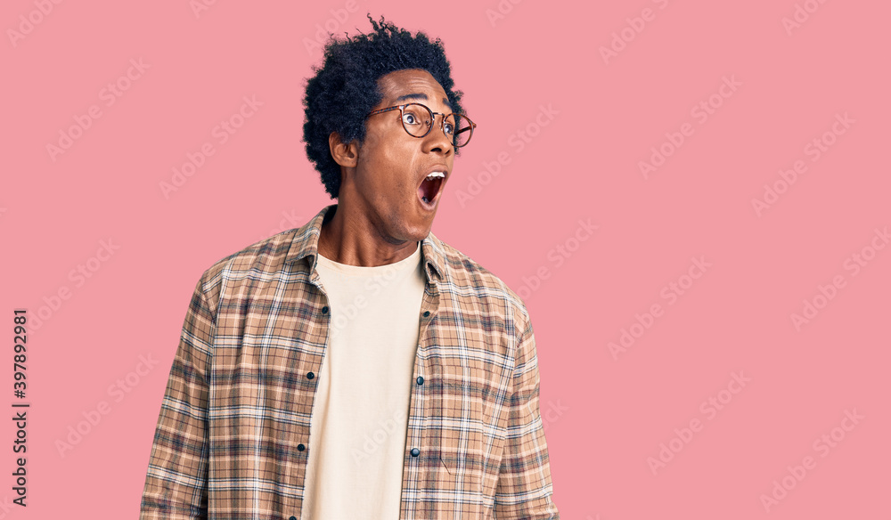 Handsome african american man with afro hair wearing casual clothes and glasses angry and mad screaming frustrated and furious, shouting with anger. rage and aggressive concept. Handsome african american man with afro hair wearing casual clothes and glasses angry and mad screaming frustrated and furious, shouting with anger. rage and aggressive concept.