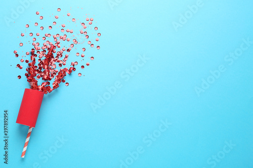 Red confetti and party cracker on light blue background, top view. Space for text