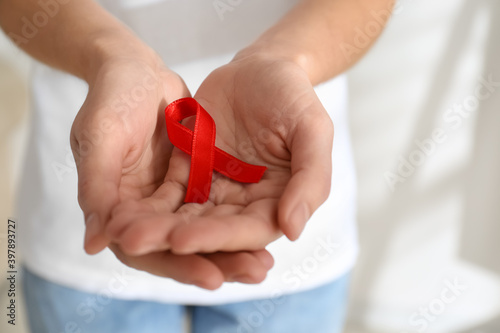 Woman holding red awareness ribbon on light background, closeup with space for text. World AIDS disease day