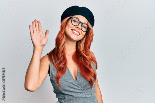 Young redhead woman wearing fashion french look with beret waiving saying hello happy and smiling, friendly welcome gesture