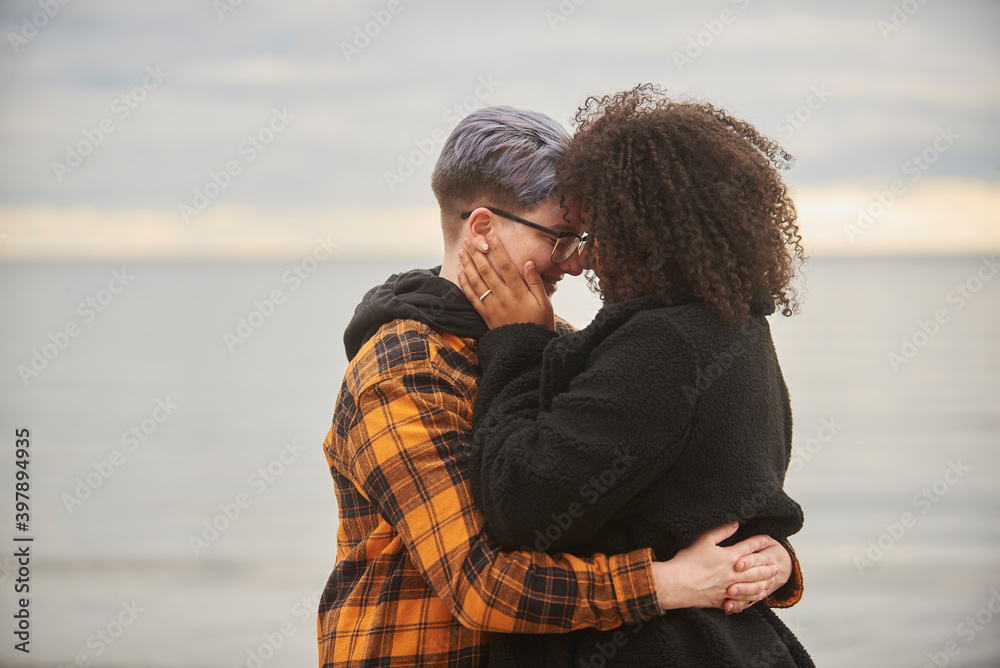Young interracial female same sex couple embracing by water. Young interracial female same sex couple embracing by water.
